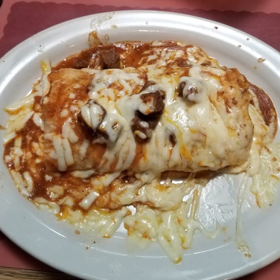 A large burrito covered in melted cheese and red sauce on a white plate.