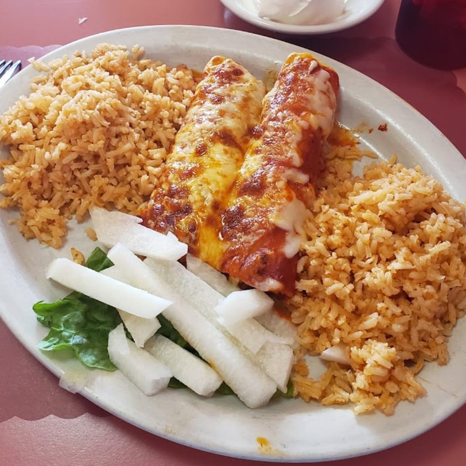 Dos Pesos Mexican Restaurant's enchiladas with rice, lettuce, and white radish slices on a white plate.