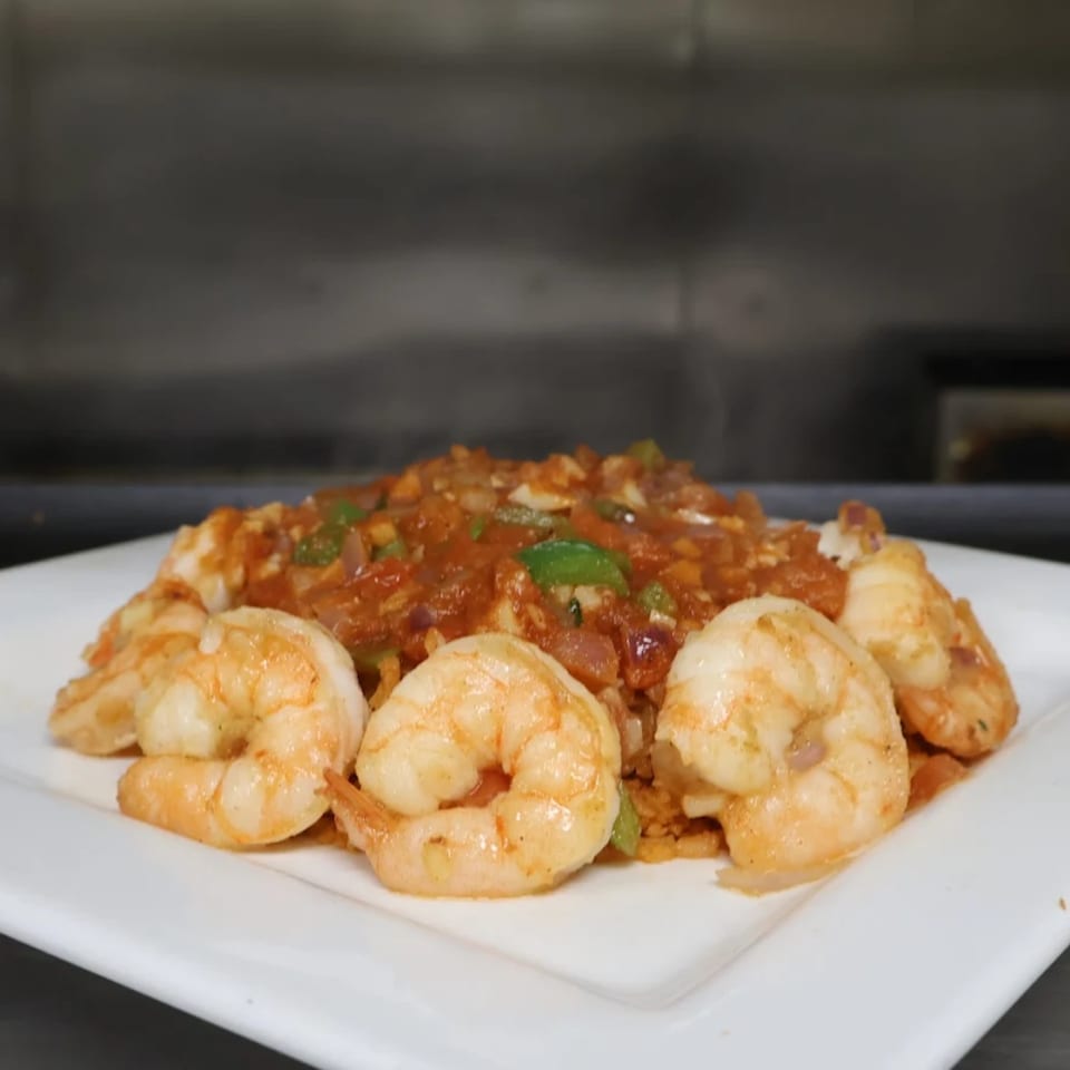 Dos Pesos Mexican Restaurant's shrimp dish with rice, red sauce, and green peppers on a white plate.