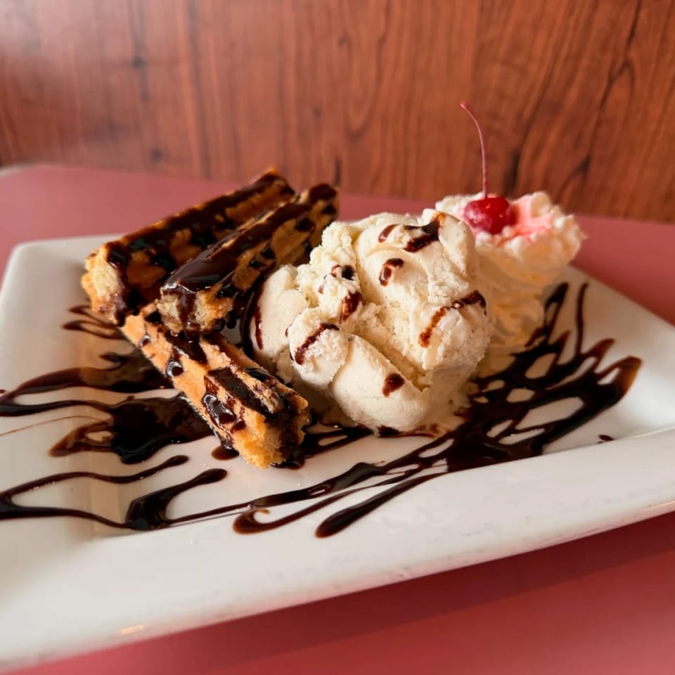 Churros drizzled with chocolate sauce, served with vanilla ice cream, whipped cream, and a cherry.